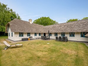 Un bâtiment à toit de chaume comprenant plusieurs pièces et une terrasse avec des sièges extérieurs.