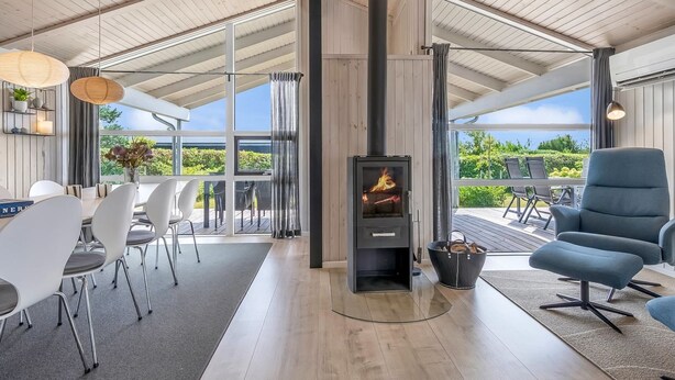 A modern interior with a wood-burning stove, a dining area with white chairs, and a view through large windows. - "Asko" - 350m from the sea by Interhome (Ebeltoft)