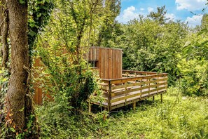 Una terraza de madera con una pequeña construcción tipo cabaña rodeada de follaje denso.