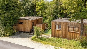 Dos cabañas de madera con un sendero de tierra que las lleva a ellas, rodeadas de árboles frondosos.