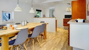 A modern kitchen with a wooden dining table, grey chairs, pendant lights, and a white countertop with a fruit bowl. - "Tannie" - 300m from the sea by Interhome (Strøby)