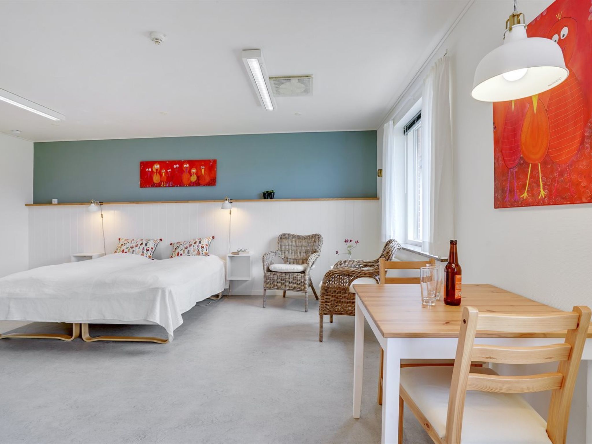 A room with a bed, a chair, a table, and a painting on the wall.