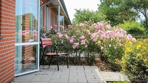 A brick building with large windows and a patio area with a chair and blooming pink flowers. - "Martinus" - 5.5km from the sea by Interhome (Tim)