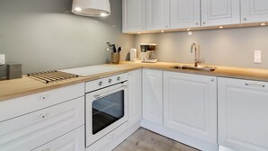 Una cocina moderna con armarios blancos, encimera de madera, horno empotrado, cafetera y lámpara colgante.