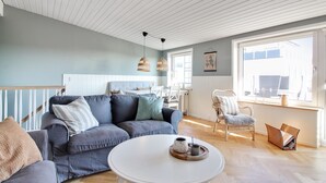 Una sala moderna con un sofá gris, una mesa de centro redonda blanca y una silla de mimbre.