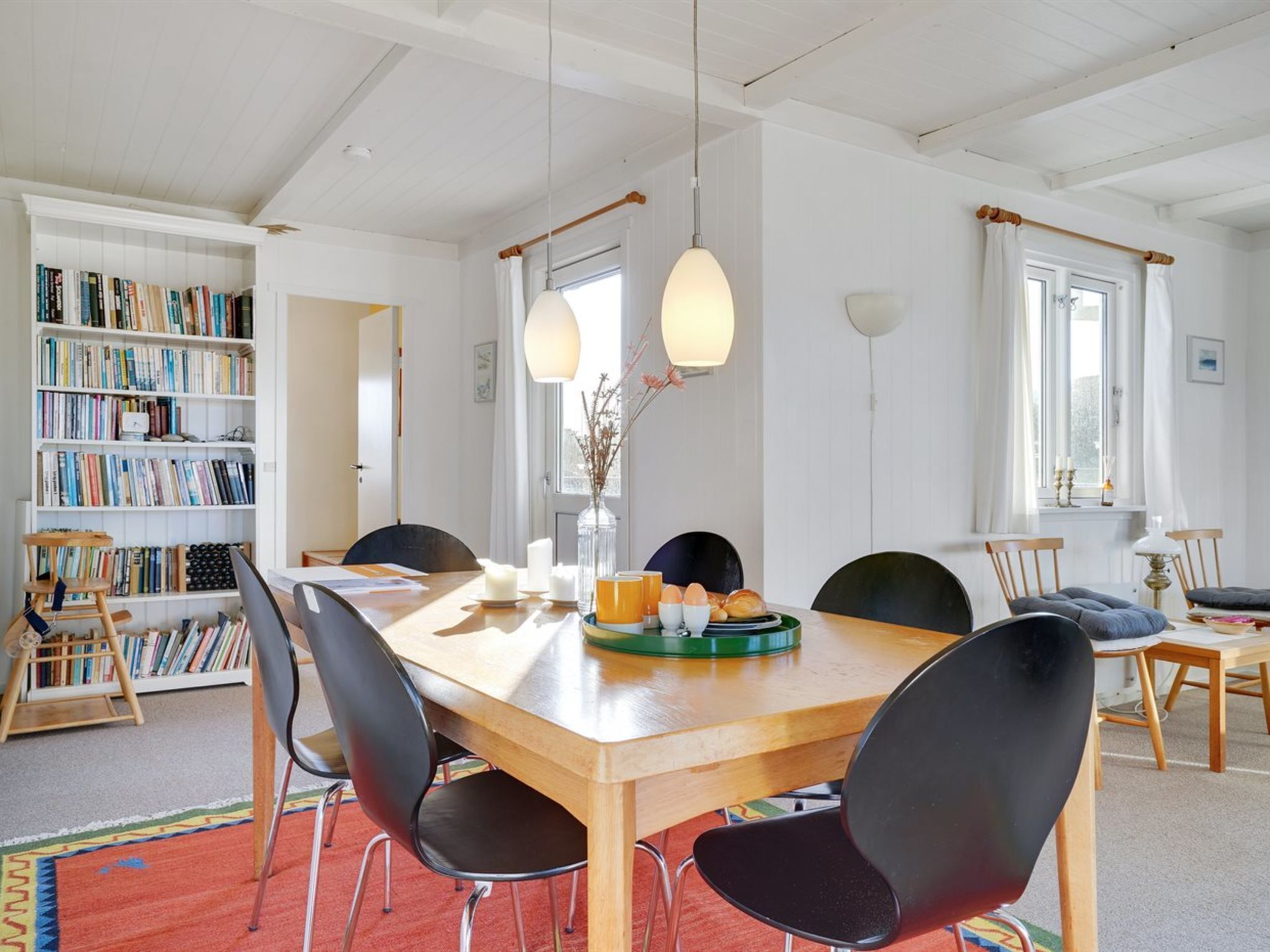 Un comedor con una mesa de madera, sillas negras y una estantería llena de libros.