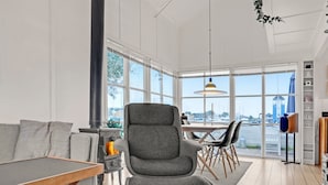 A modern interior with a grey upholstered chair, a wooden dining table, and a large window offering a view of the marina.