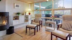 Een gezellige woonkamer met een open haard, houten vloeren en een groot raam met uitzicht op de omgeving.