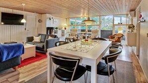 Een moderne woonkamer met een houten plafond, een eethoek met een witte tafel en een keuken op de achtergrond.