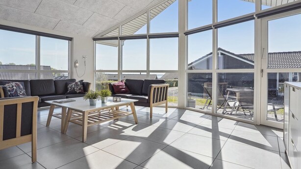 A spacious sunroom with large windows, a wooden coffee table, a sofa, and a chair.