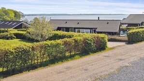 A row of cottages with a gravel driveway, surrounded by well-maintained hedges and trees, overlooking a body of water.