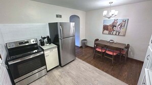 A compact kitchen with a refrigerator, oven, and microwave. There's a dining table with chairs and a trash can.