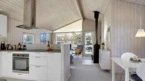 Et moderne køkken med en central ø, et spiseområde med bord og stole, samt udsigt gennem en glasdør til en udendørs terrasse.