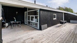 En moderne bygning med en træterrasse, et overdækket udendørs siddeområde og et stort vindue.