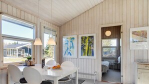 Et moderne spiseområde med et hvidt bord og stole, store vinduer og abstrakt kunst på væggene.