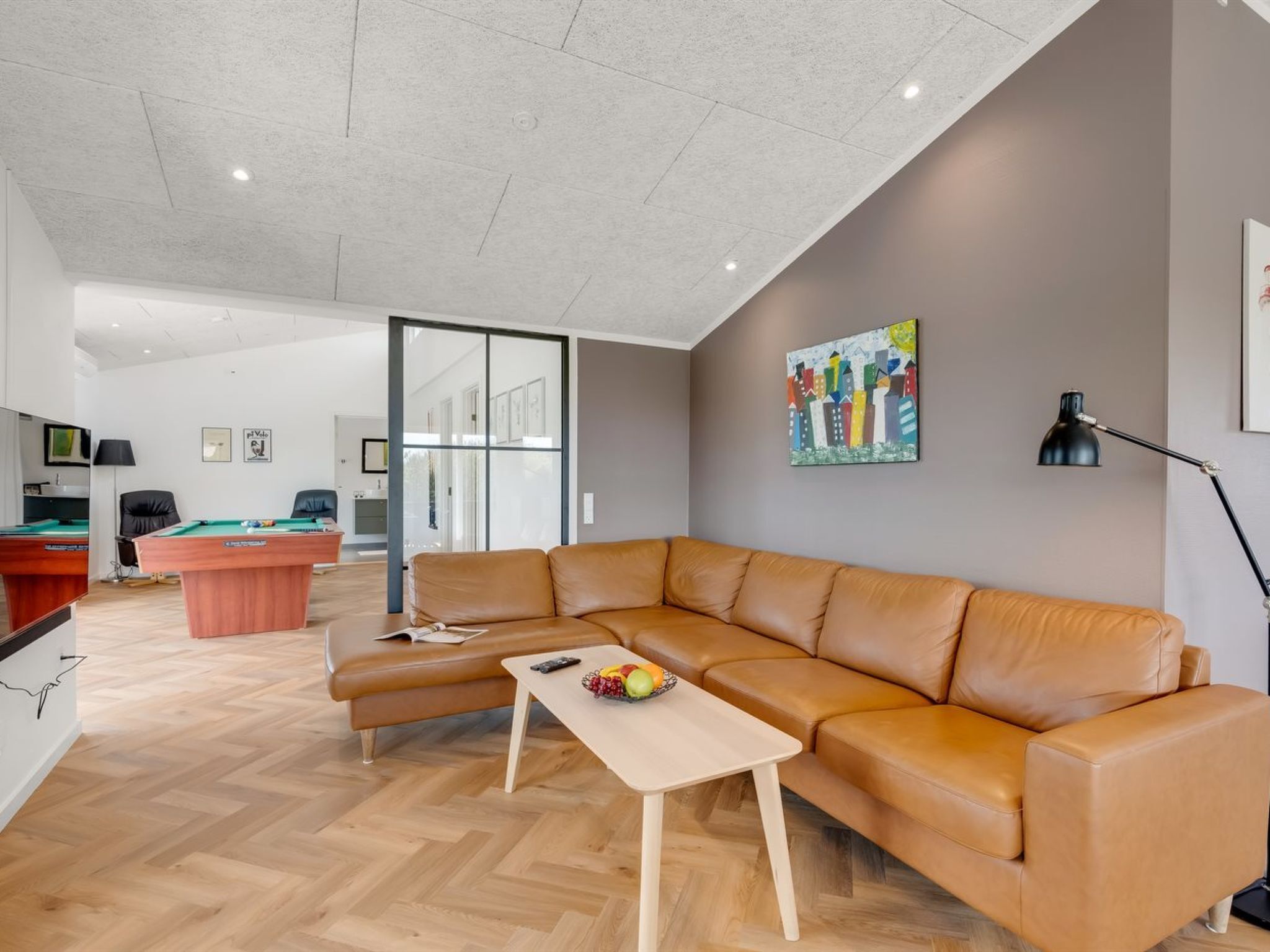 A modern living room with a leather sofa, a wooden coffee table, and a colorful cityscape painting on the wall.