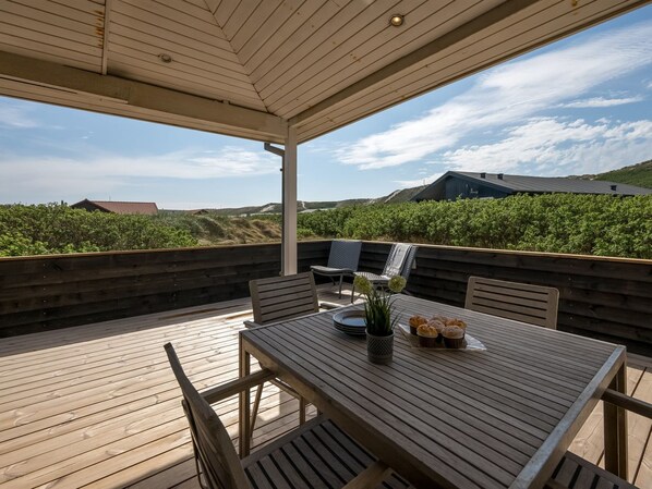 A wooden deck with a table and chairs, a potted plant, and a view of the landscape.