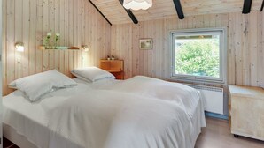 A bedroom with a wooden ceiling, a bed with white bedding, a window with a view of greenery, and a shelf with decorative items. - "Thorgot" - 400m from the sea by Interhome (Sydals)