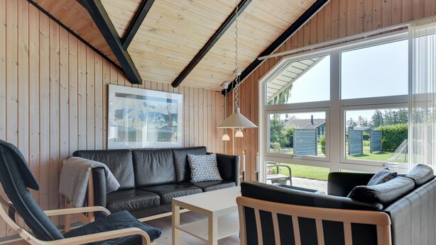A cozy room with a wooden ceiling, a black leather sofa, a wooden chair, and a large window offering a view of the outdoors. - "Thorgot" - 400m from the sea by Interhome (Sydals)