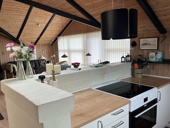 A modern kitchen with a wooden ceiling, a white countertop, a built-in stove, and a window with blinds.