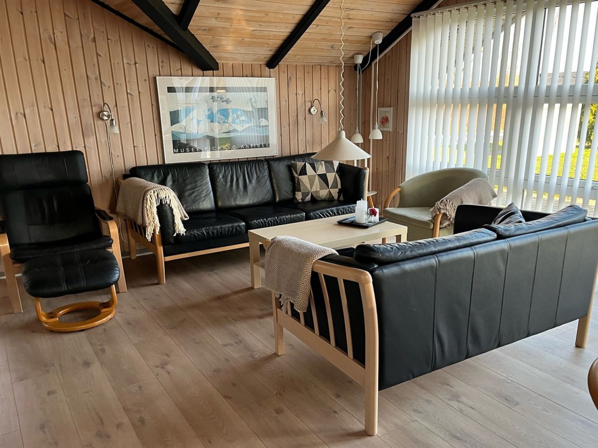 Ein modernes Wohnzimmer mit einem schwarzen Ledersofa, einem Holztisch, einem schwarzen Lederstuhl und einem Bettgestell aus Holz.