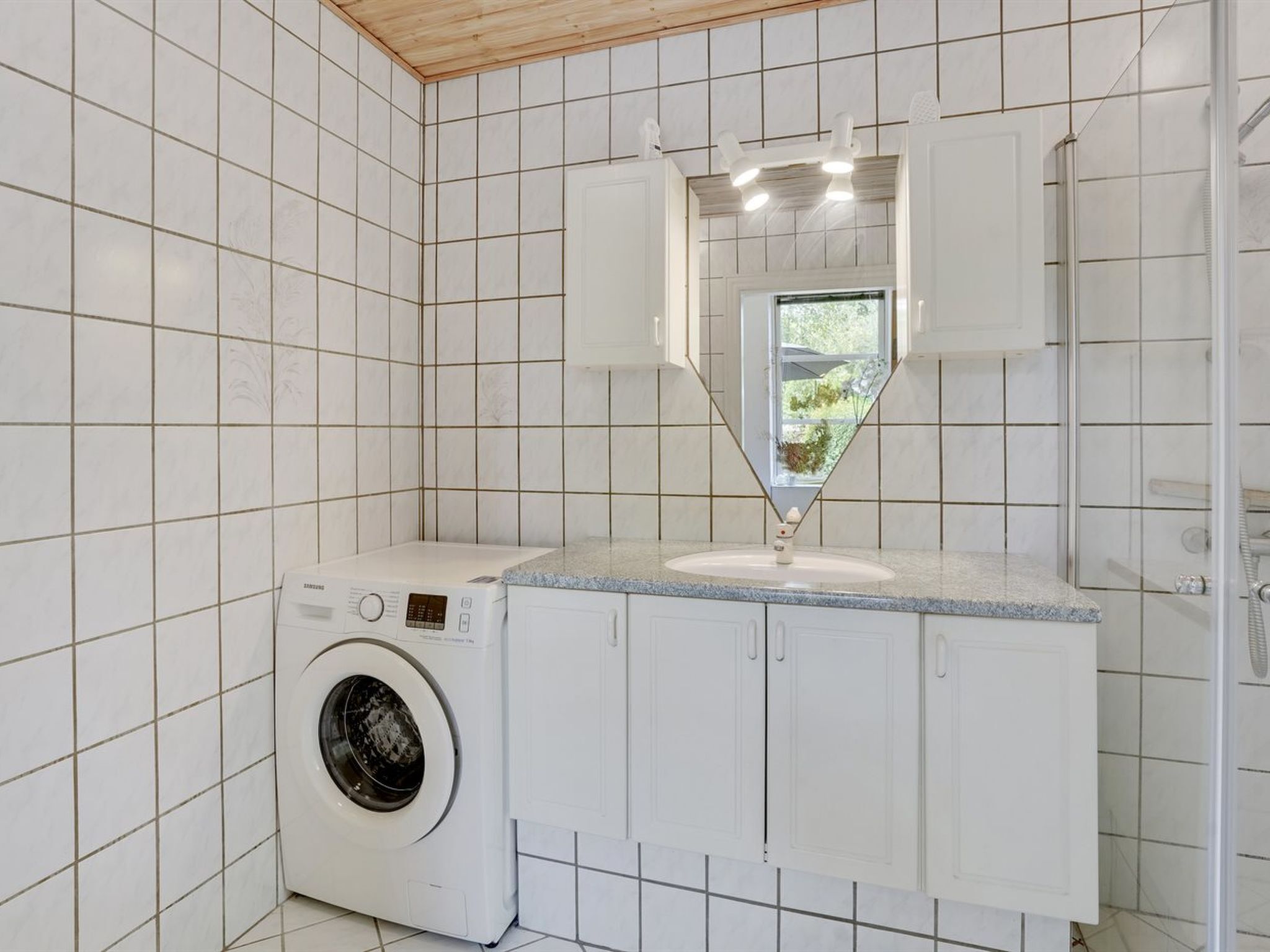 A compact laundry room with a washing machine, a sink, and a mirror.