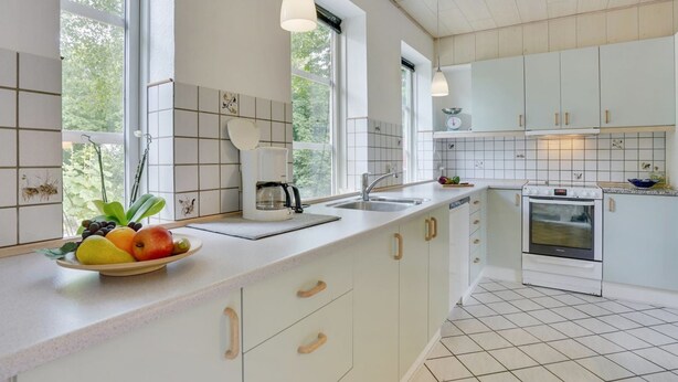 Une cuisine moderne avec des meubles blancs, un grand îlot central agrémenté d’un panier de fruits, une machine à café et une cuisinière.