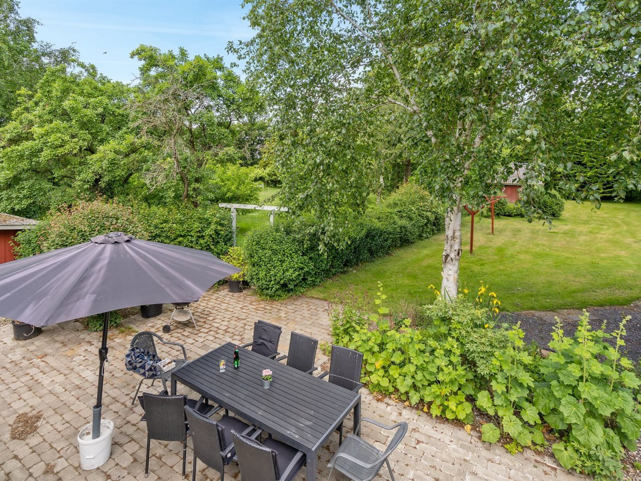 En uteplats med ett bord och stolar, omgiven av frodig grönska och en välskött gräsmatta.