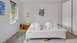 Une chambre à coucher avec un lit, des tables de chevet, une fenêtre et des œuvres d’art accrochées aux murs.