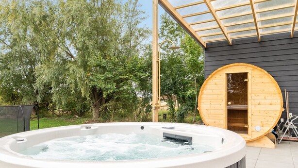 Un bain à remous avec une structure extérieure en bois et un sauna à parois vitrées.