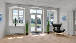 Une pièce spacieuse avec un plancher en bois, de grandes fenêtres en arc de cercle, une chaise noire et des plantes en pot.