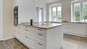 Une cuisine moderne avec des meubles blancs, un îlot central et une vue sur l’extérieur grâce à de grandes fenêtres.