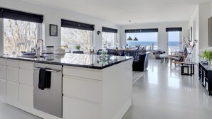 Een moderne keuken met een centraal eiland, grote ramen en uitzicht op zee.