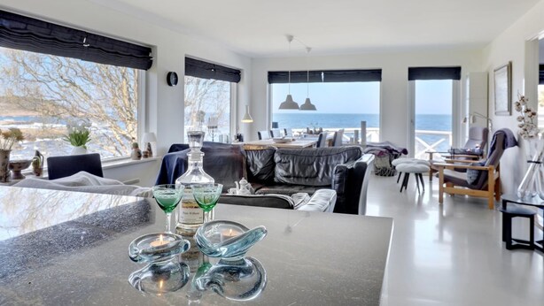 Een moderne woonkamer met uitzicht op zee, een bar met een fles wijn, en een gezellige zithoek.