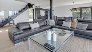 Ein modernes Wohnzimmer mit einem großzügigen Ecksofa, einem Glastisch und einer Treppe, die in eine obere Etage führt.