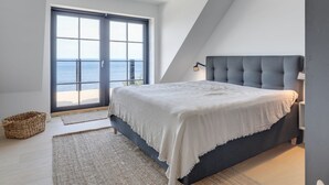 Ein Schlafzimmer mit großem Fenster, einem Bett, einer Nachttischlampe und einem gewebten Korb.