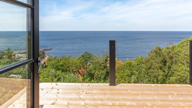 Blick vom Balkon auf eine Küstenlandschaft bei klarem Himmel und Meer.