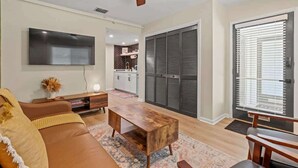 A modern living room with a sofa, coffee table, and TV. There is a kitchen in the background and a sliding door closet.