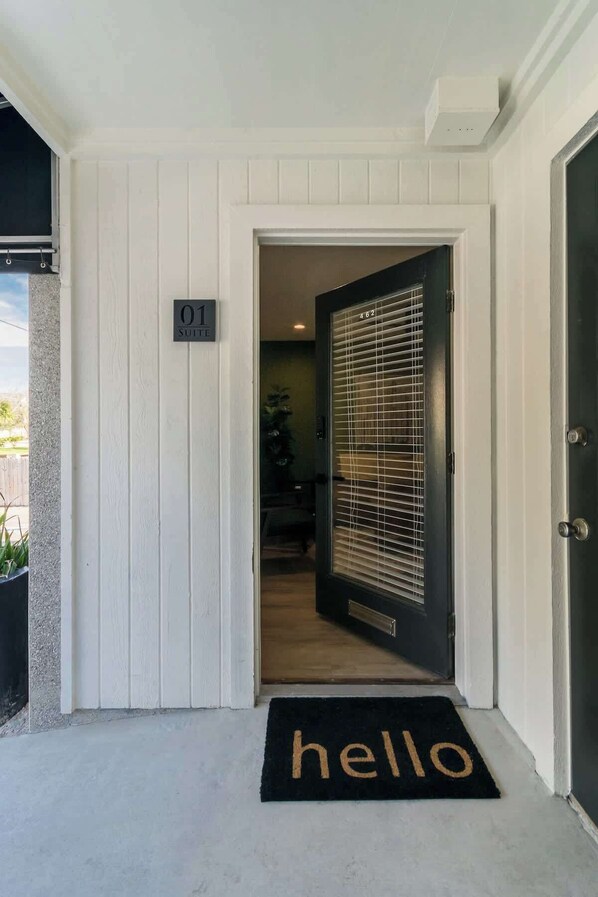 A white exterior wall with a door labeled "01 Suite" and a black doormat with "hello" on it.