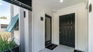 A clean, modern entrance with a black door, a 'hello' mat, and a blue awning.