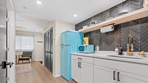 A modern kitchen with white cabinets, a blue refrigerator, a microwave, and a sink with a gold faucet.