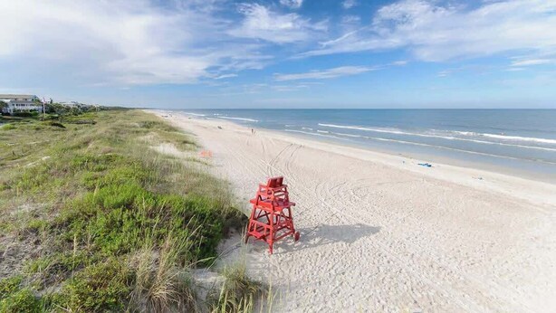 A beach with a lifeguard tower, sandy shore, and grassy dunes.
