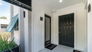 A clean, modern entrance with a black door, a 'hello' mat, and a blue awning.