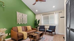 Una sala de estar con una pared verde, un sofá marrón, un sillón azul, una mesa de centro de madera y un ventilador de techo.