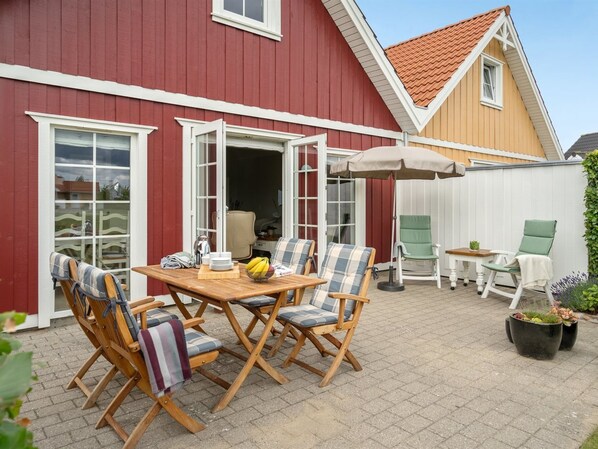 A patio with a wooden table and chairs, a small umbrella, and potted plants.