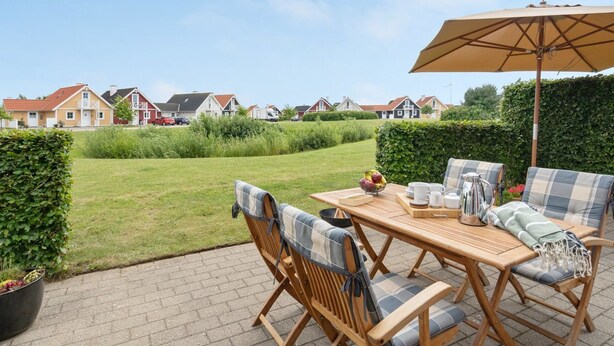 A patio with a wooden table and chairs, an umbrella, and a view of houses in the background. - "Eike" - 250m from the sea by Interhome (Brenderup Fyn)