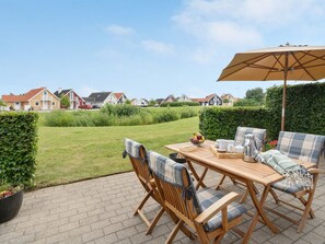 A patio with a wooden table and chairs, an umbrella, and a view of houses in the background.