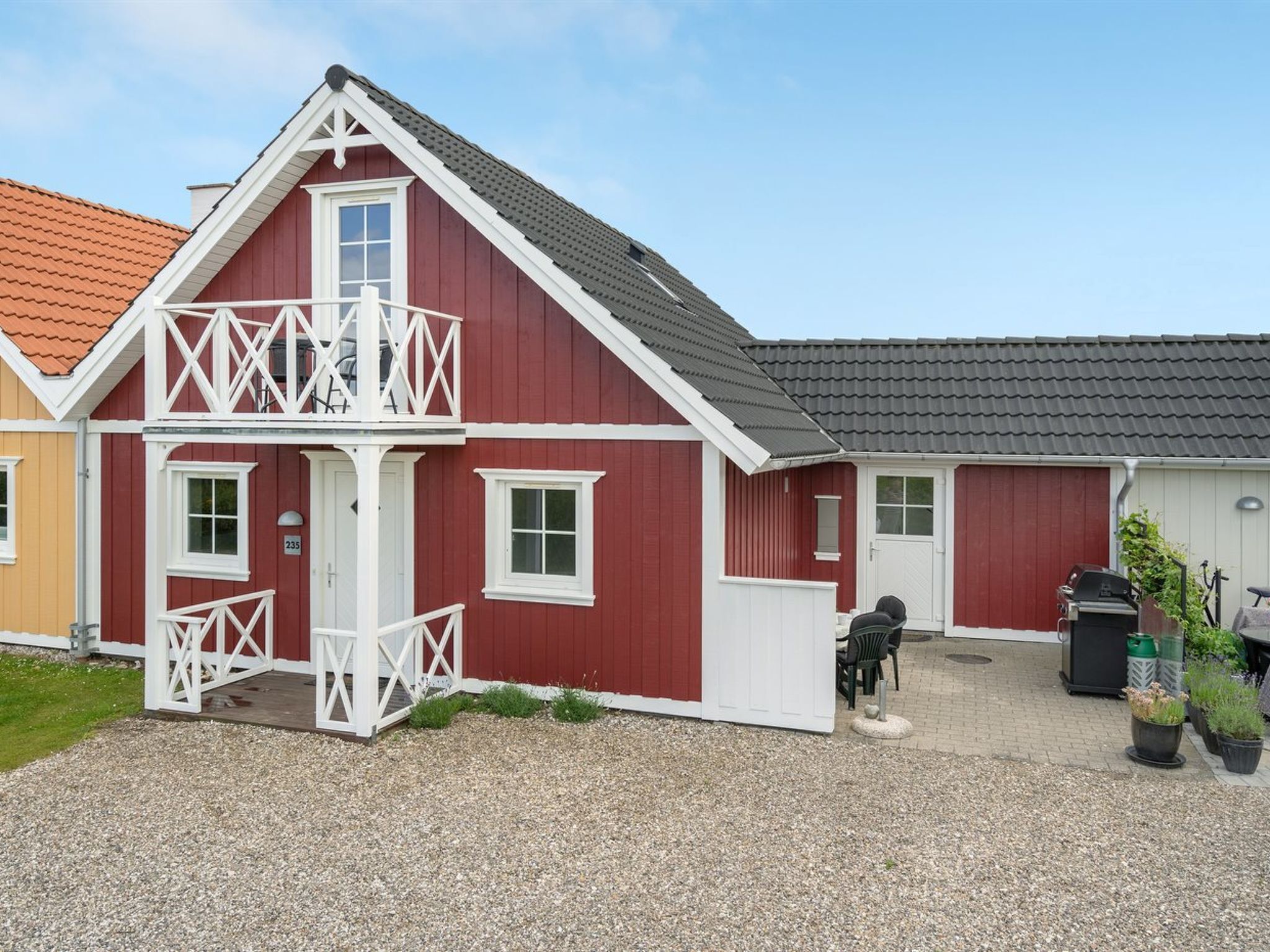 A red building with a white balcony, a gravel driveway, and a barbecue area.