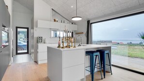A modern kitchen with a large island, bar stools, and a view of the countryside. - "Gunborg" - 400m from the sea by Interhome (Sjølund)