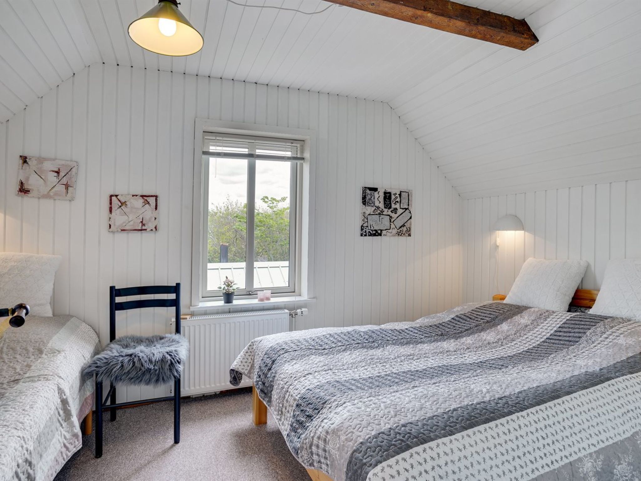 A cozy bedroom with two beds, a chair, a radiator, and artwork on the walls.